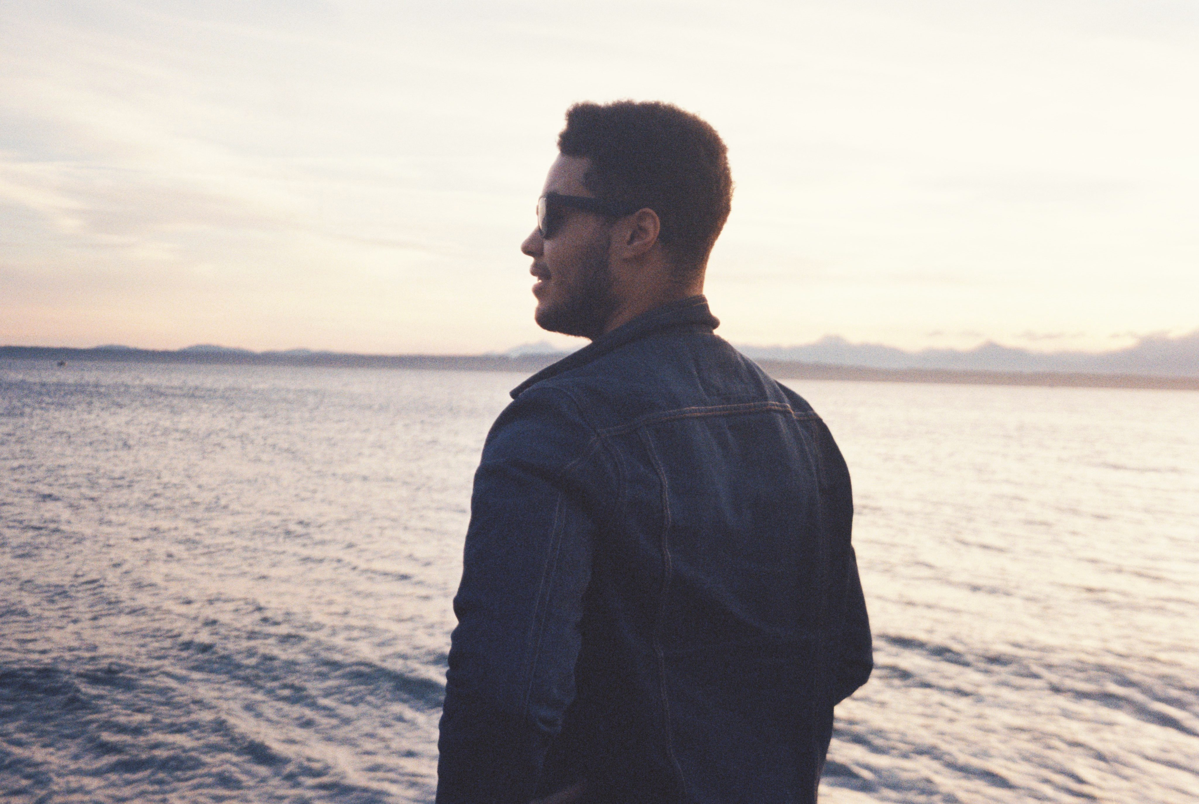 Kwesi Phillips in denim jacket by the ocean at golden hour